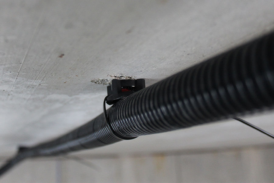 Close-up of a black cable securely mounted to a ceiling using a small plastic clip, ensuring a neat and organized appearance.